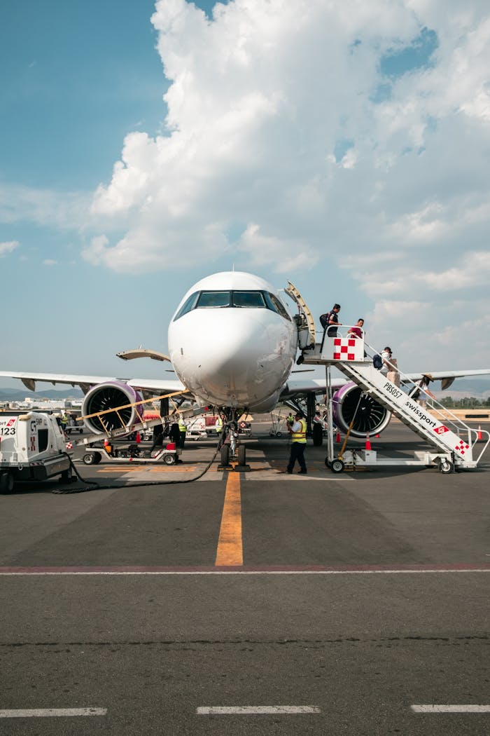 A large passenger airplane on the tarmac with boarding stairs and ground staff nearby.